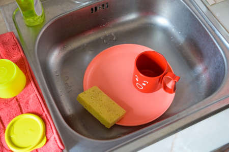 Bright plastic dishes in sink with spongeの写真素材