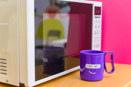 Plastic cup with smiling face next to microwaveの写真素材