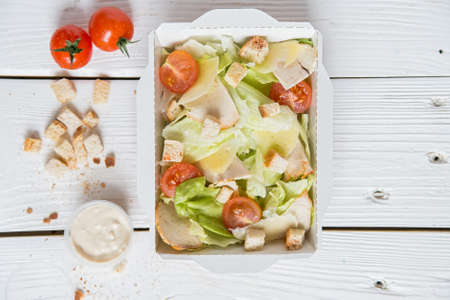 Caesar salad in box on white wooden surfaceの写真素材