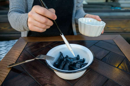 Woman puts butter on black vareniki in bowlの写真素材