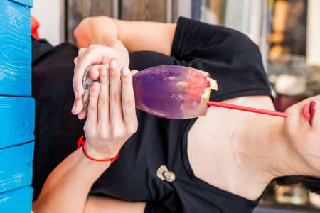 Close up young beautiful woman holding glass with dark cocktail with grapefruit and straw in...