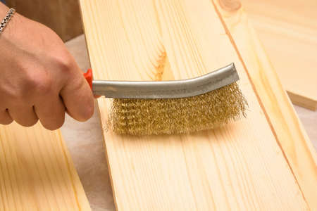 Hand with metal brush brushes wooden plankの写真素材