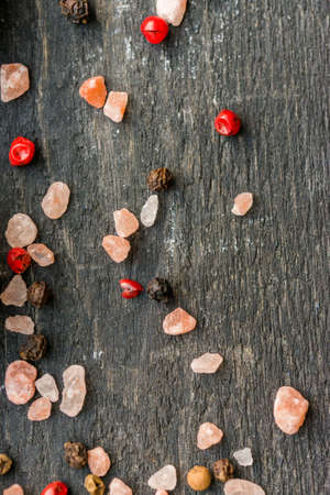 Pink salt grains and peppercorn on wooden table