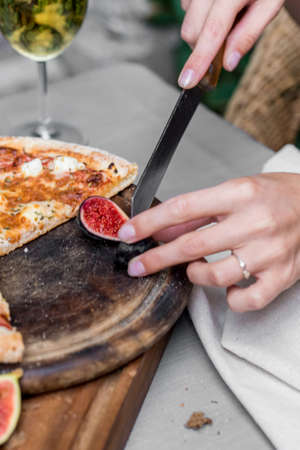Close-up of woman's hands cutting fig on wooden board with pizza on it