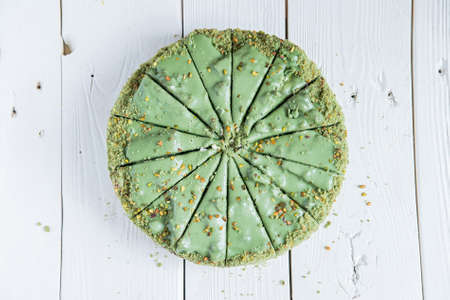 Pistachio cake sliced on white wooden background