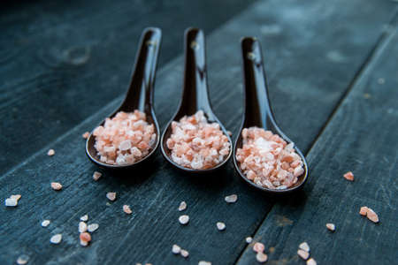 Close up picture of three spoons with rough pink salt on dark wooden backgroundの写真素材