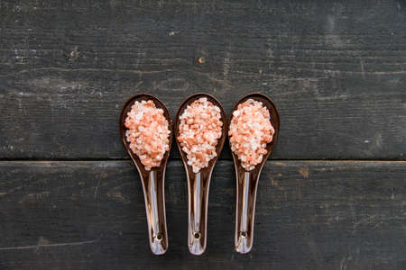 Top view of three spoons with rough pink salt on dark wooden backgroundの写真素材