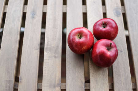 Three dark red apples on wooden surface top viewの写真素材
