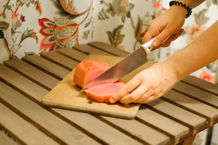 Woman cutting fresh salmon fillet on wooden boardの写真素材