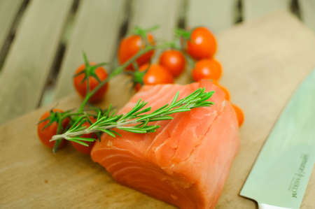 Salmon fillet and cherry tomatoes on cutting boardの写真素材