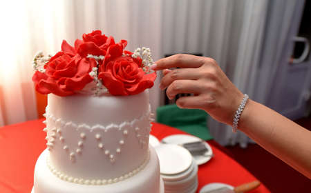 Female hand adjusts flowers on wedding cake