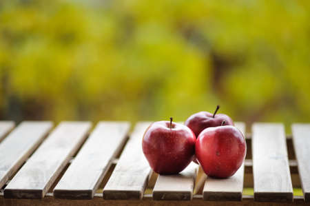 Close up image of three ripe fresh apples on wooden planks outdoors with blurred green backgroundの写真素材