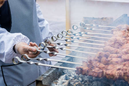 Close up man's hand adjusting meat grilled on skewersの写真素材