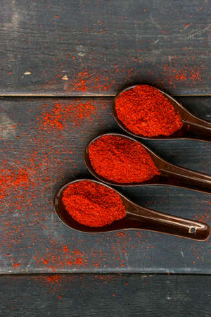 Top view three plastic spoons filled with red paprika spice on dark wooden backgroundの写真素材