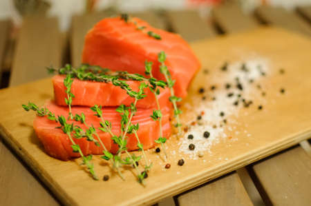 Close up salmon fillet with black pepper, herbs and salt on wooden boardの写真素材