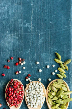 Three wooden spoons with pink and white peppercorn and cardamom on dark backgroungの写真素材