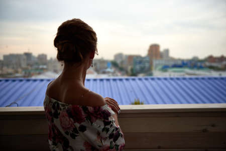 Back view of a dressed-up woman looking at the city from balconyの写真素材