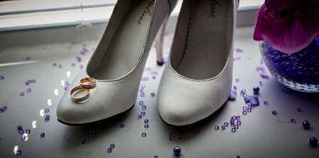 Close up two golden rings lying on white shoes with heelsの写真素材