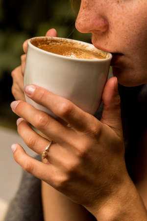 Pretty girl wrapped in blanket drinks coffee