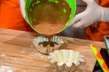 Hands pour dough in cupcake mold