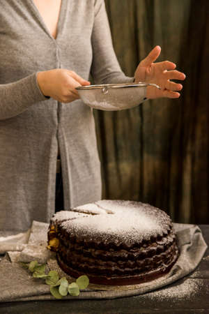 Woman covers chocolate cake with sugar powder