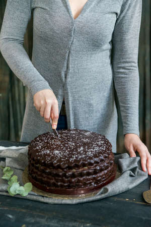 Woman cuts chocolate cake close. Dark tones