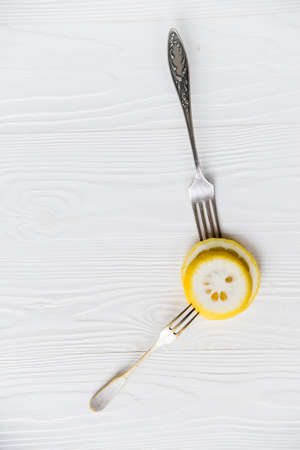 Slices of lemon and forks on white wooden surfaceの写真素材