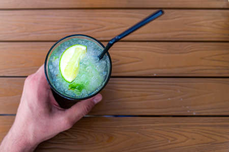 Hand holds mojito cocktail with lime and mint in glass on wooden tableの写真素材
