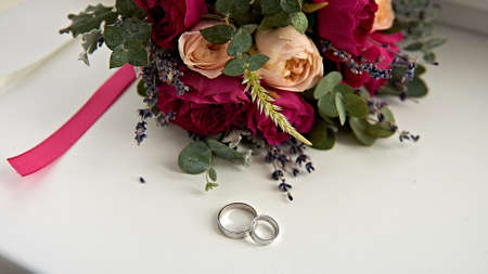 Wedding rings and brides bouquet on white