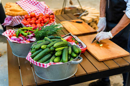 Chef slices fresh vegetables for salad in outdoor kitchenの写真素材