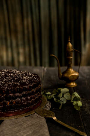 Close up delicious chocolate cake, small decorative kettle and spoon on vintage wooden table. Selective focus.の写真素材