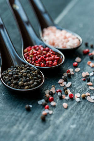 Studio shot of three spoons with rough pink salt, black and pink peppercorns on dark wooden backgroundの写真素材