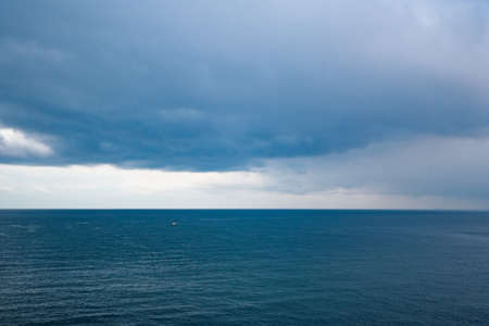 View of calm sea and grey cloudy sky and a boatの写真素材