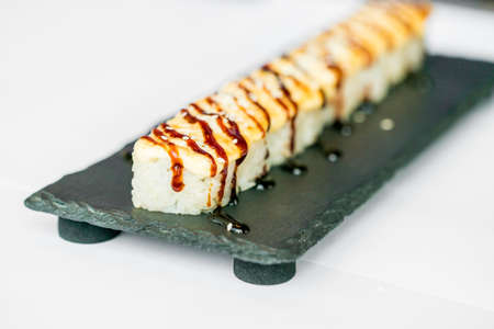 Freshly cooked uncut sushi roll on black boardの写真素材