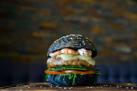 Black burger with prawns on wooden boardの写真素材