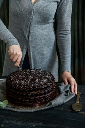 Woman cuts chocolate cake close. Dark tonesの写真素材