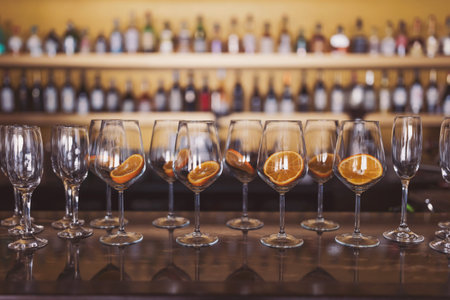 Row of wine glasses with slices of orange on the bar counter.