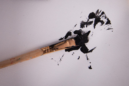 Close up of paint brush with black paint splatter on white canvasの写真素材