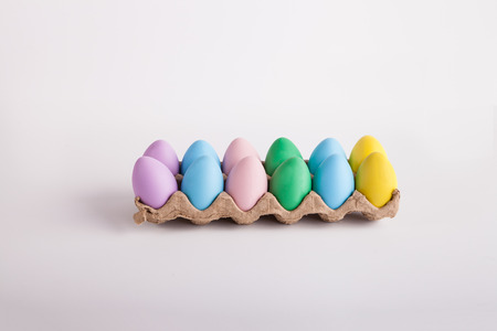 Carton of pastel colored Easter eggs on solid background