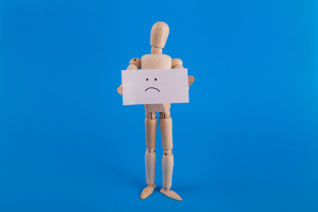 sad face sign held by emotionless wooden jointed doll