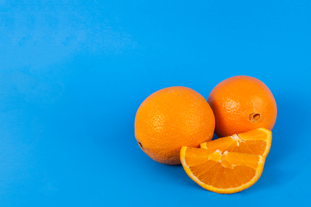two whole navel oranges two sweet orange slices on a solid blue background composed right lower in the frameの写真素材