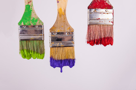 Three painters paintbrushes wet red green purple paint dripping
