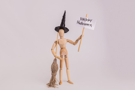 Halloween witch holding a Happy Halloween picket sign holding a broom wearing a black pointed hat jointed dummy doll on solid backgroundの写真素材