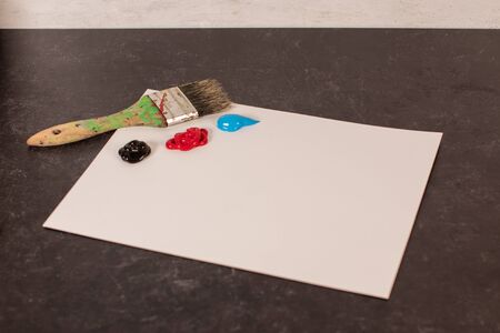 Blank white paper with wet piles of blue black and red paint dry paint brushesの写真素材