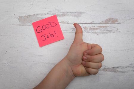 human hand giving a thumbs up with good job note card