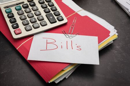 The word bills on white note card laying on stack of unpaid bills calculater in backgroundの写真素材