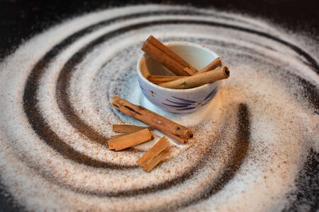 Bowl of fresh raw whole cinnamon sticks swirled white sugar caneの写真素材