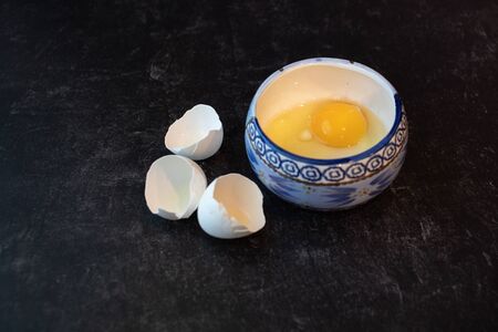 Whole egg yolk in bowl with cracked eggshells on the side breakfast ingredients