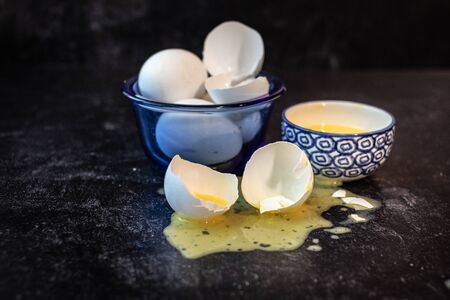 Cracked and whole raw eggs scrabbled eggs in a bowl and spilled on tableの写真素材