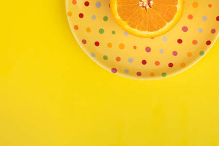 Bright yellow background dead space with poke a dot plate half an orangeの写真素材